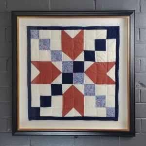 A quilt is displayed in a frame on the wall.