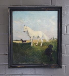 white horse against blue skies. ground is lit in background a light yellow, foreground is shaded greens. two dark dogs accompany the horse. This is framed in an antique rustic black scoop frame.