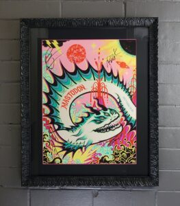 Mastadon concert poster of a serpent/dragon - stylized - in teals, black, and white. The serpent in atop a yellow, pink, and orange background. The print is matted with black matboard and has a frame with shapes that are similar to the spine of the serpent.