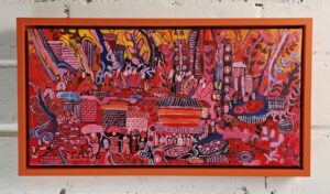 Painting from Africa of a busy village with large foliage and people bustling. The colors are psychedelic in reds, yellows, orange, and purple. This is framed in a solid orange floater frame.